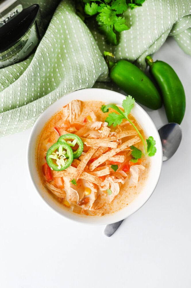 Slow cooker creamy chicken enchilada soup in white bowl topped with jalapeños and cilantro