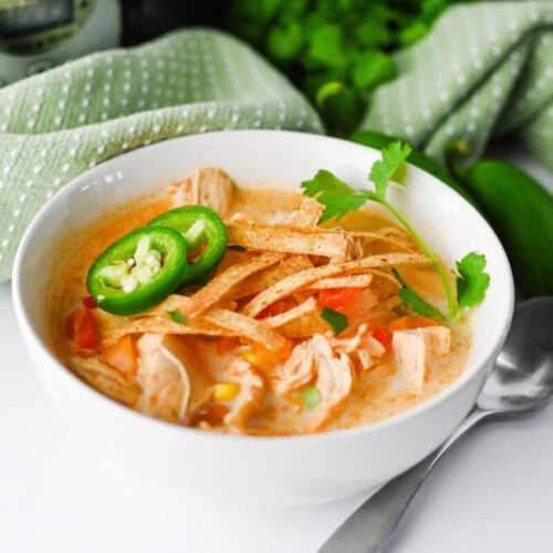 Slow cooker creamy chicken enchilada soup in white bowl with jalapeño and cilantro garnish