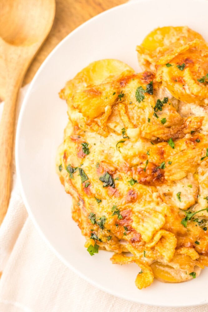 Cheesy French onion potato casserole with golden crispy layers, melted cheese, and fresh parsley garnish on white plate