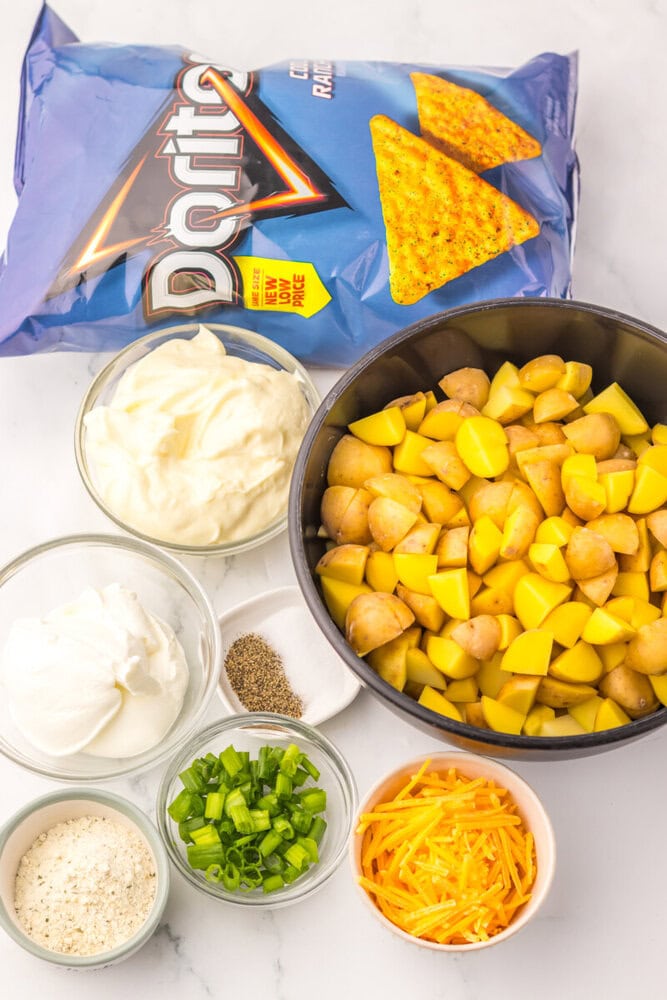 Cool Ranch Dorito Potato Salad ingredients laid out including Doritos chips, cooked vegetables, mayo, sour cream, cheese, and seasonings