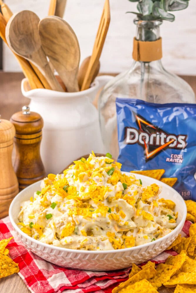 Cool Ranch Dorito potato salad in white bowl topped with crushed chips and green onions, styled with Doritos bag and wooden kitchen accessories