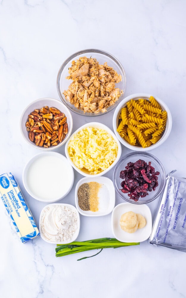 Cranberry white cheddar chicken pasta ingredients laid out in bowls overhead view including pasta corn nuts cranberries flour butter and seasonings