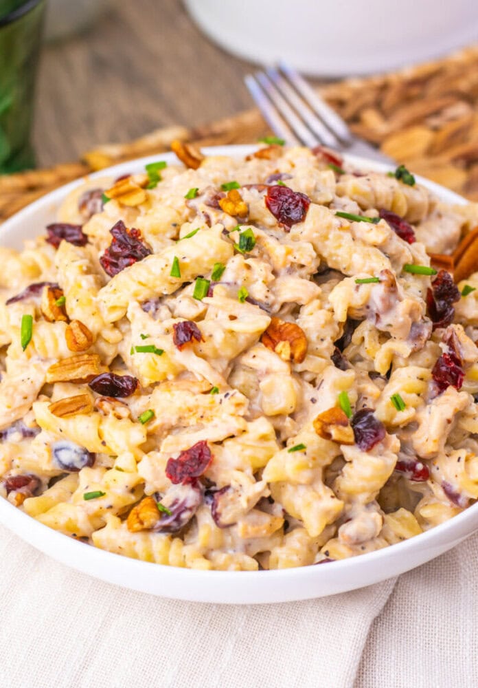 Cranberry white cheddar chicken pasta salad with cranberries, toasted pecans, and chives on a white plate