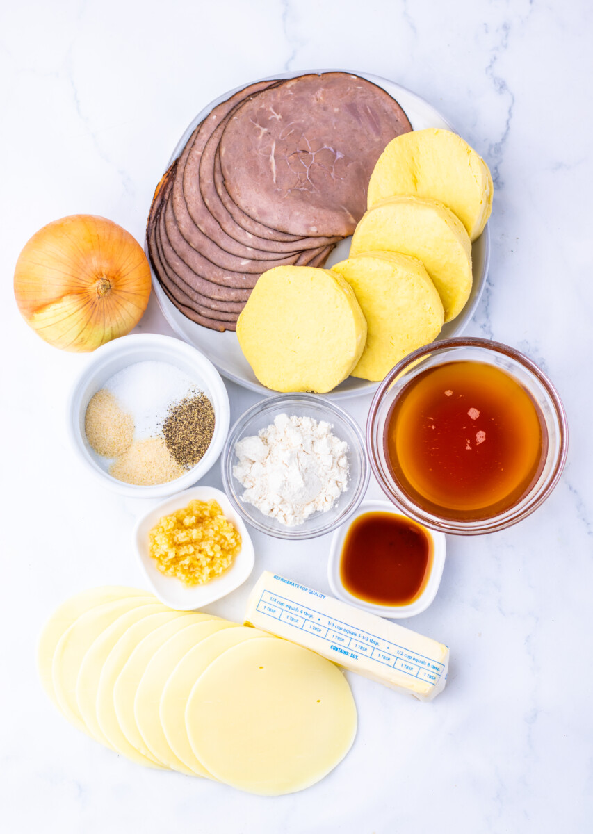 French Dip Biscuit Casserole ingredients overhead flat lay including deli meat slices, potatoes, cheese, onion, spices and sauces