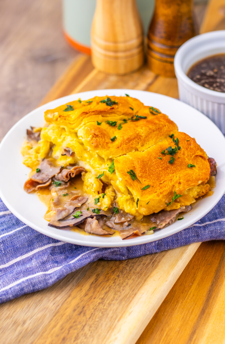 French Dip Biscuit Casserole with golden biscuit topping and roast beef, plated and ready to serve with dipping sauce