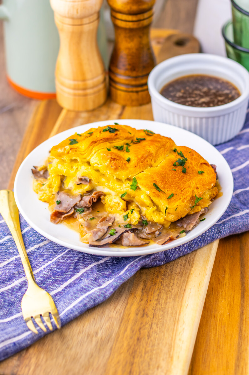 French Dip Biscuit Casserole with fluffy omelet, ham, and melted cheese garnished with parsley, served with gravy