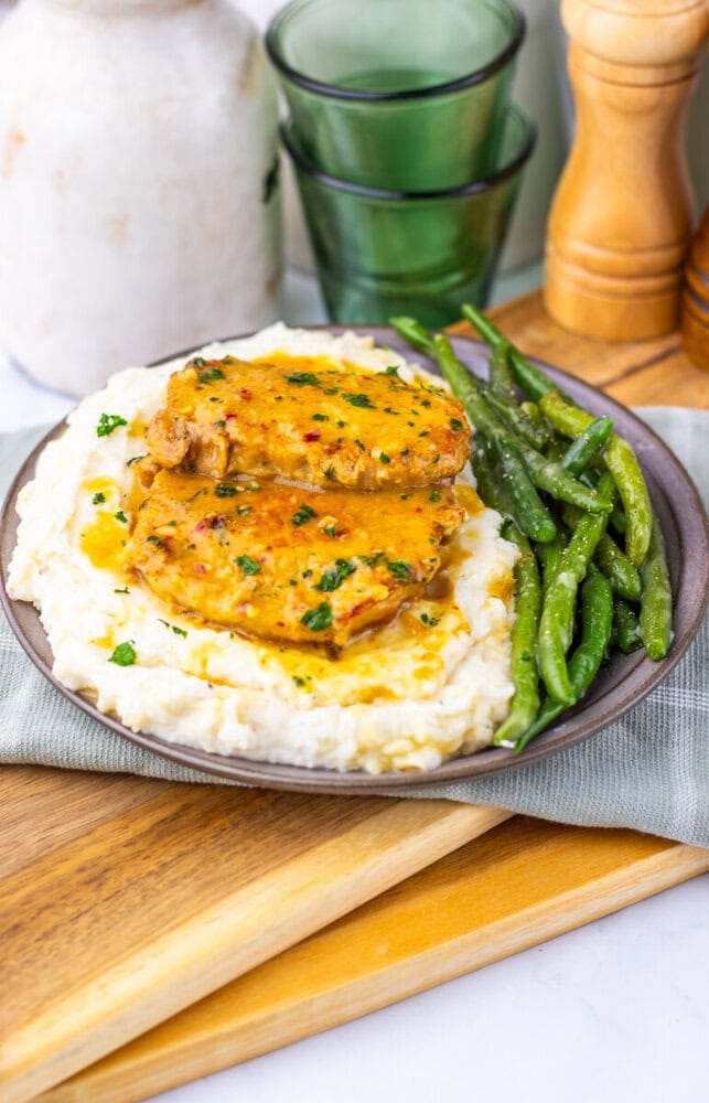 Maple Dijon Pork Chops plated with mashed potatoes and green beans, garnished with fresh herbs