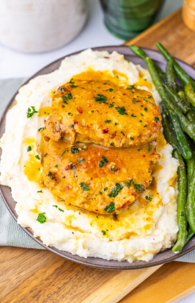 Maple Dijon pork chops plated on mashed potatoes with green beans and herb garnish
