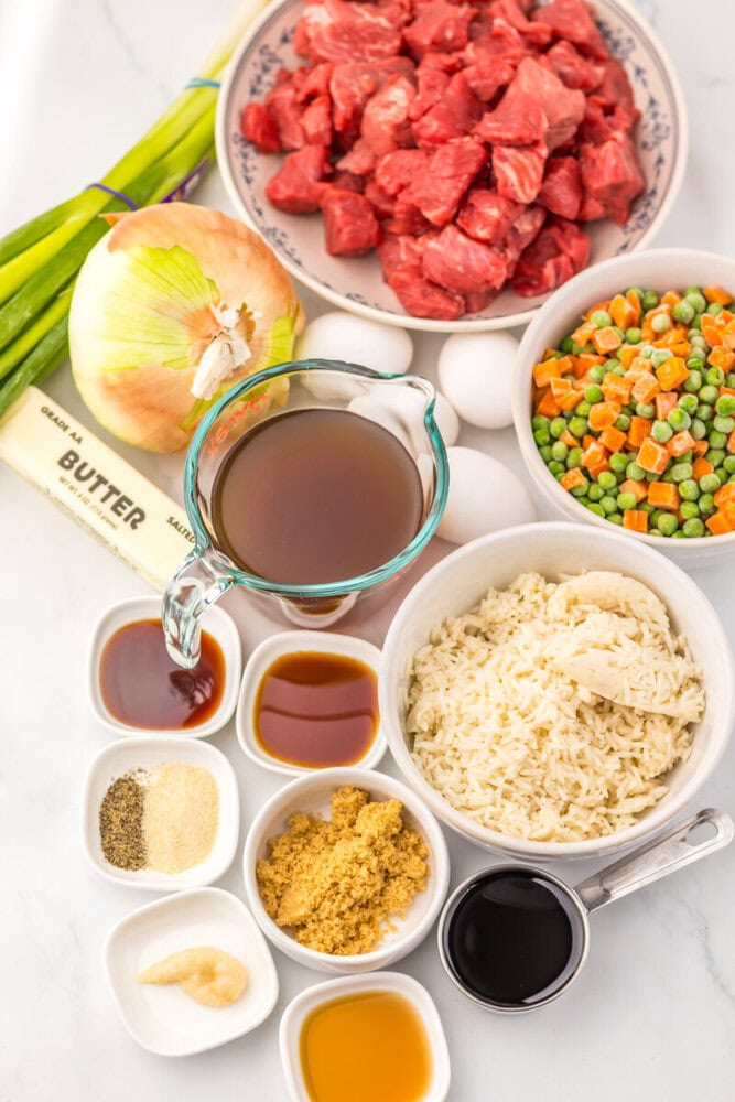 Slow cooker beef fried rice ingredients laid out in bowls including raw beef, rice, mixed vegetables, onion, and seasonings