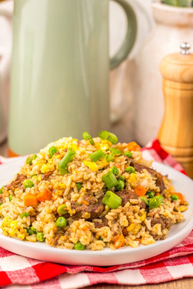 Slow cooker beef fried rice served on white plate with green onions, corn, and carrots garnish