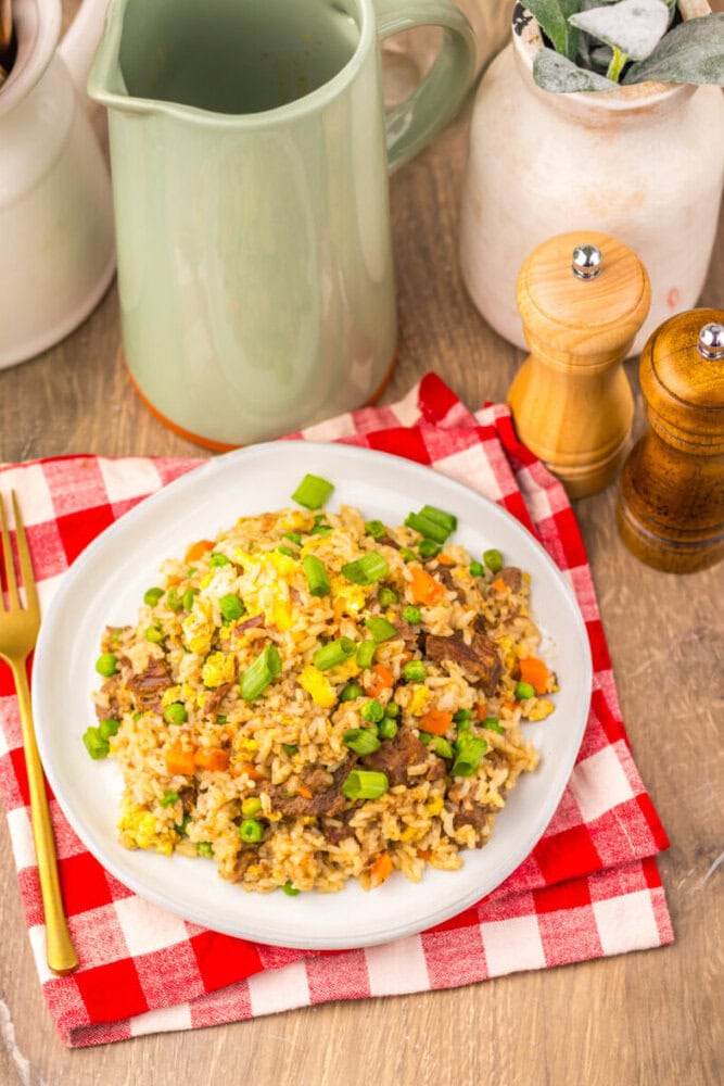 Slow cooker beef fried rice plated on white dish with green onion garnish and wooden utensils