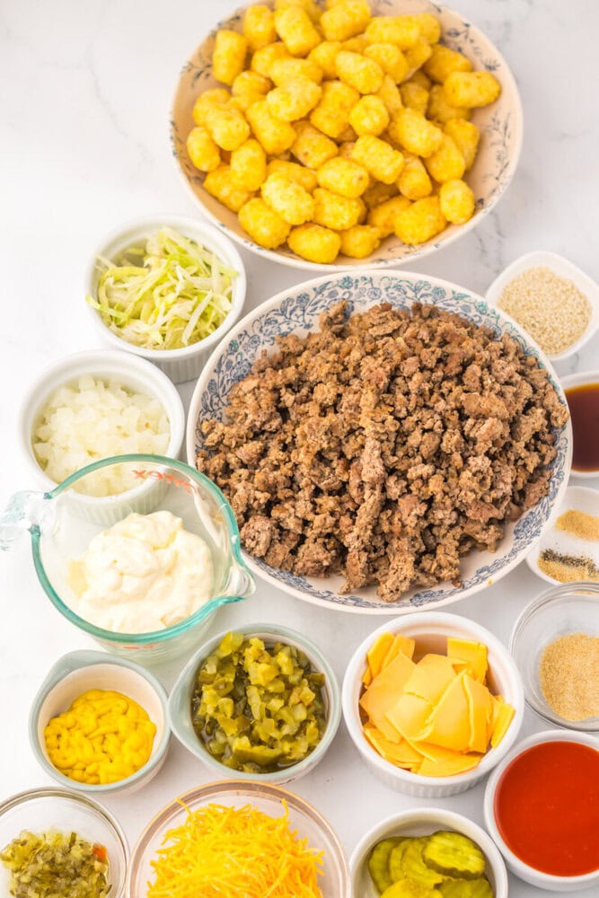Slow Cooker Big Mac Tater Tot Casserole ingredients laid out overhead including ground beef, tater tots, cheese, mayo, pickles, and seasonings