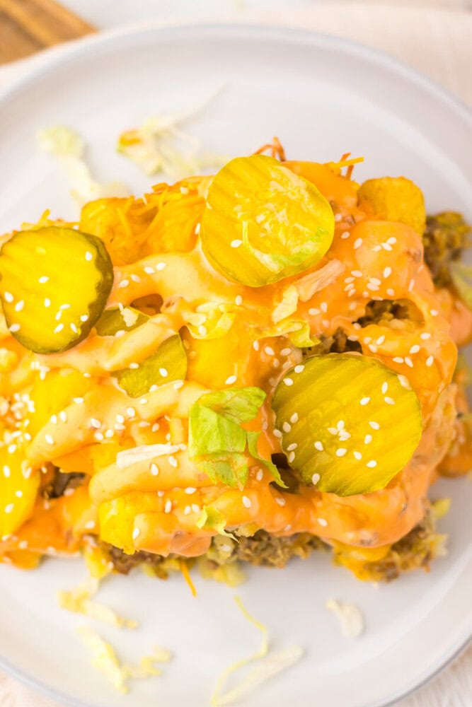 Slow cooker big mac tater tot casserole with cheese, pickles, sesame seeds and green onions on white plate