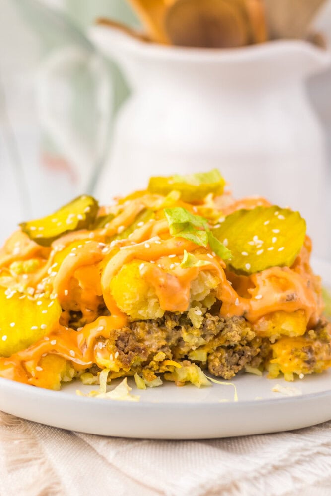 Slow cooker big mac tater tot casserole plated on white dish with melted cheese and pickles