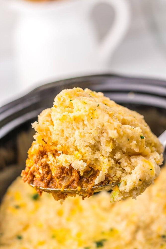 Slow cooker sloppy joe bake with golden cornbread topping and meat filling on serving spoon