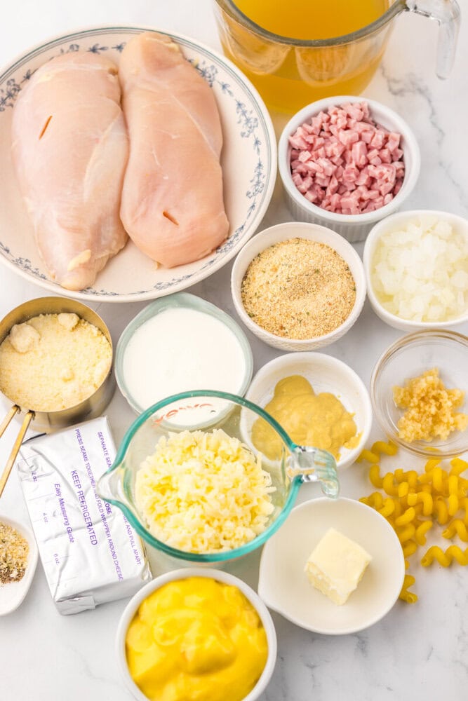 Slow cooker chicken cordon bleu pasta ingredients laid out including raw chicken breasts, ham, corn, cheese, breadcrumbs and seasonings