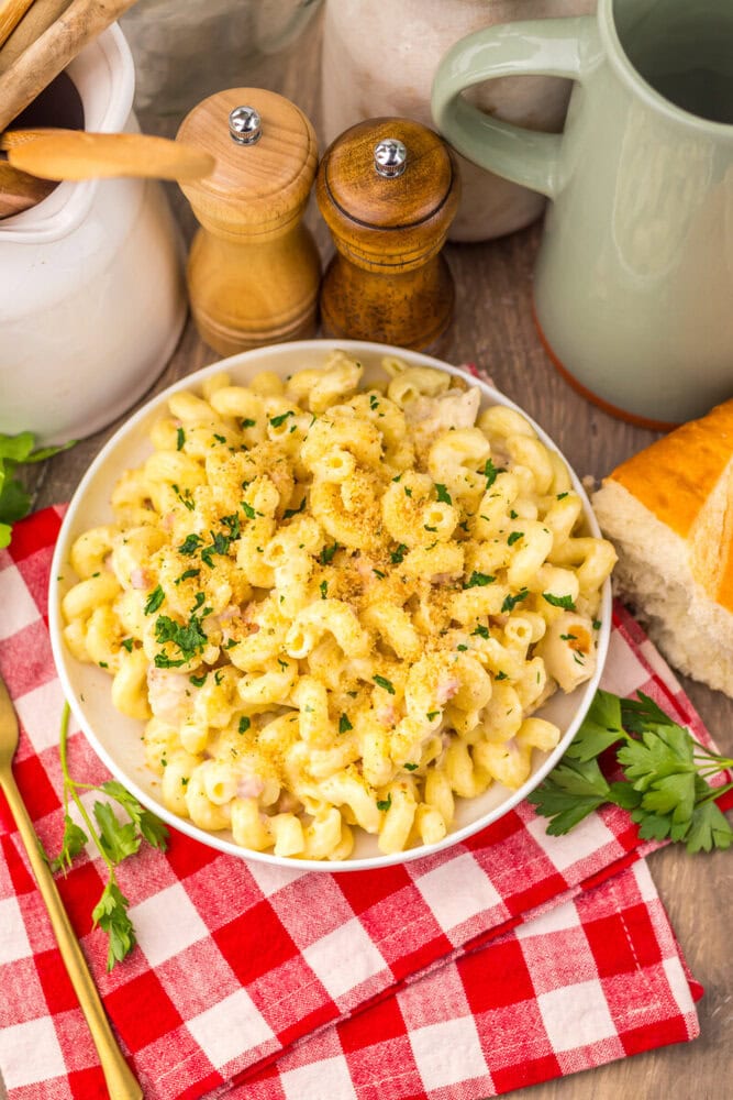 Creamy slow cooker mac and cheese garnished with parsley in white bowl with salt and pepper mills