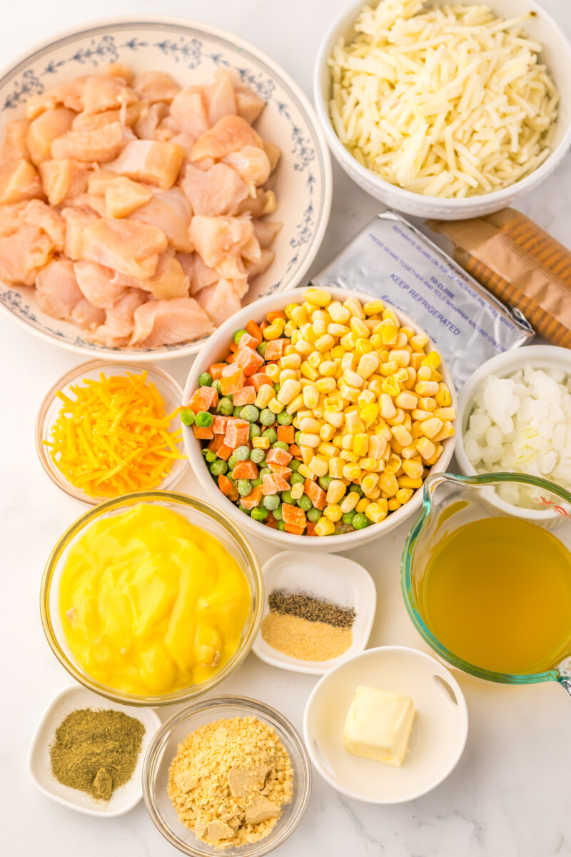 Slow cooker chicken pot pie hash brown casserole ingredients laid out overhead including chicken, hash browns, vegetables, cheese, and seasonings
