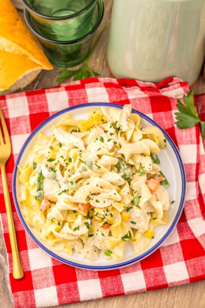 Slow cooker chicken pot pie pasta with creamy sauce, vegetables, and fresh herbs in a white bowl