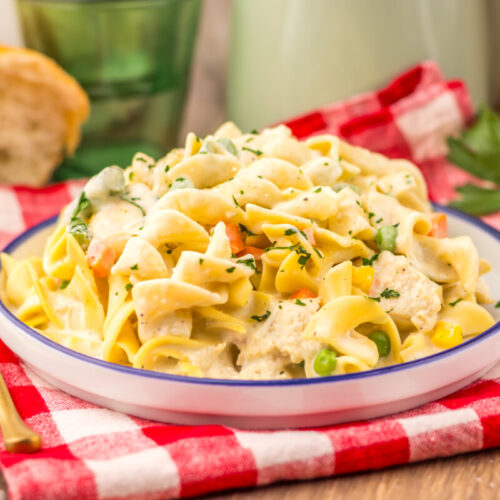 Slow cooker chicken pot pie pasta with egg noodles, vegetables, and herbs garnish on a plate with checkered napkin