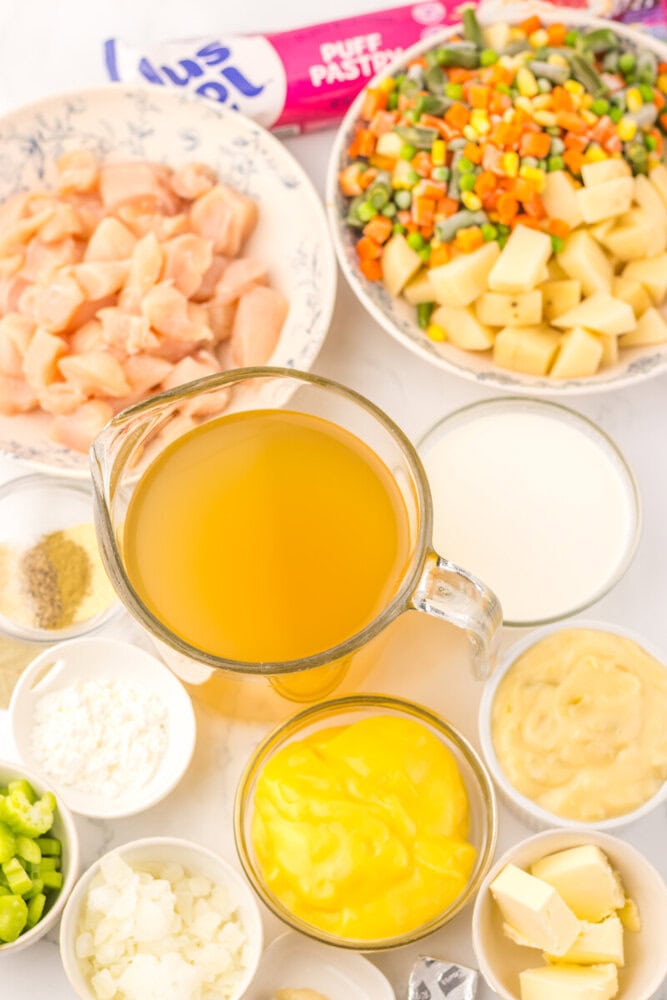 Slow cooker chicken pot pie soup ingredients laid out including diced chicken, mixed vegetables, broth, cream, and seasonings