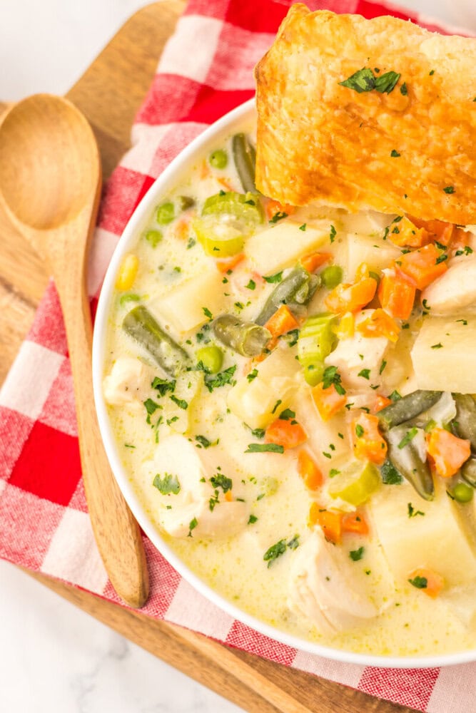 Slow cooker chicken pot pie soup in white bowl with pastry crust, garnished with herbs and vegetables