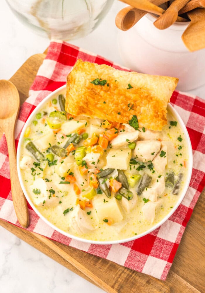 Slow cooker chicken pot pie soup in white bowl with puff pastry topping and fresh garnish
