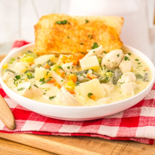 Slow cooker chicken pot pie soup in white bowl with bread garnish and fresh herbs