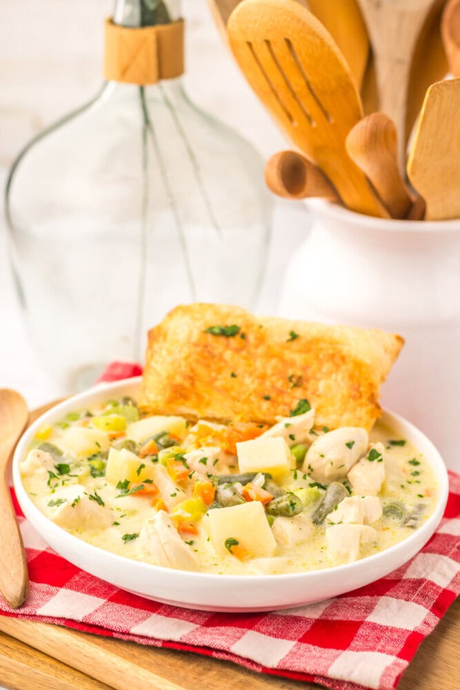 Slow cooker chicken pot pie soup in white bowl with biscuit topper, creamy broth with potatoes and vegetables
