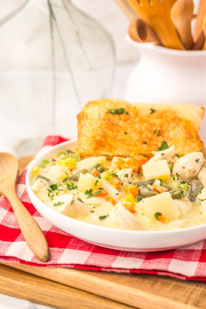 Slow cooker chicken pot pie soup in white bowl with diced potatoes, vegetables, and herbs, served with toasted bread