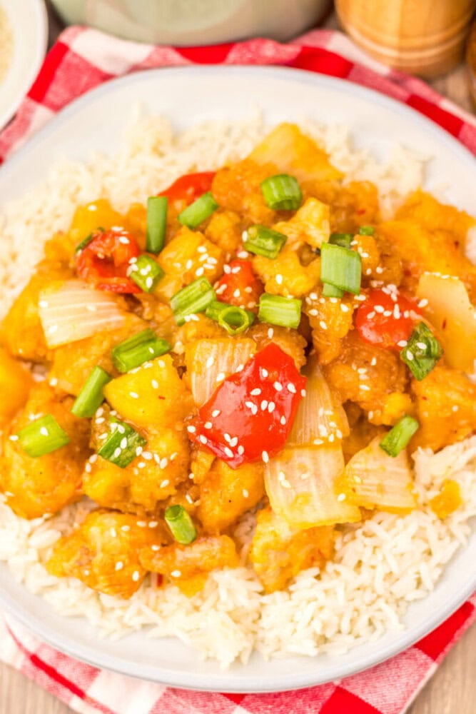 Slow cooker sweet fire chicken with pineapple and bell peppers over rice, garnished with sesame seeds and scallions