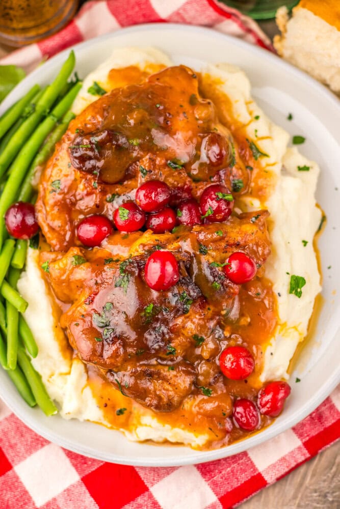Slow cooker cranberry BBQ chicken with mashed potatoes, green beans, and cranberry garnish on white plate