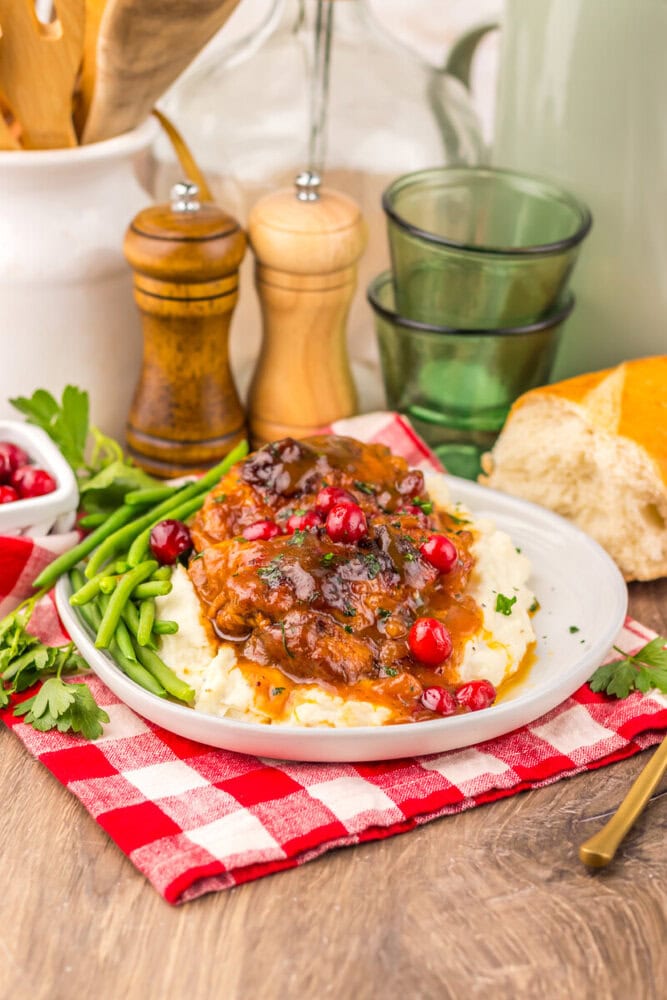 Slow cooker cranberry BBQ chicken served over mashed potatoes with green beans on white plate