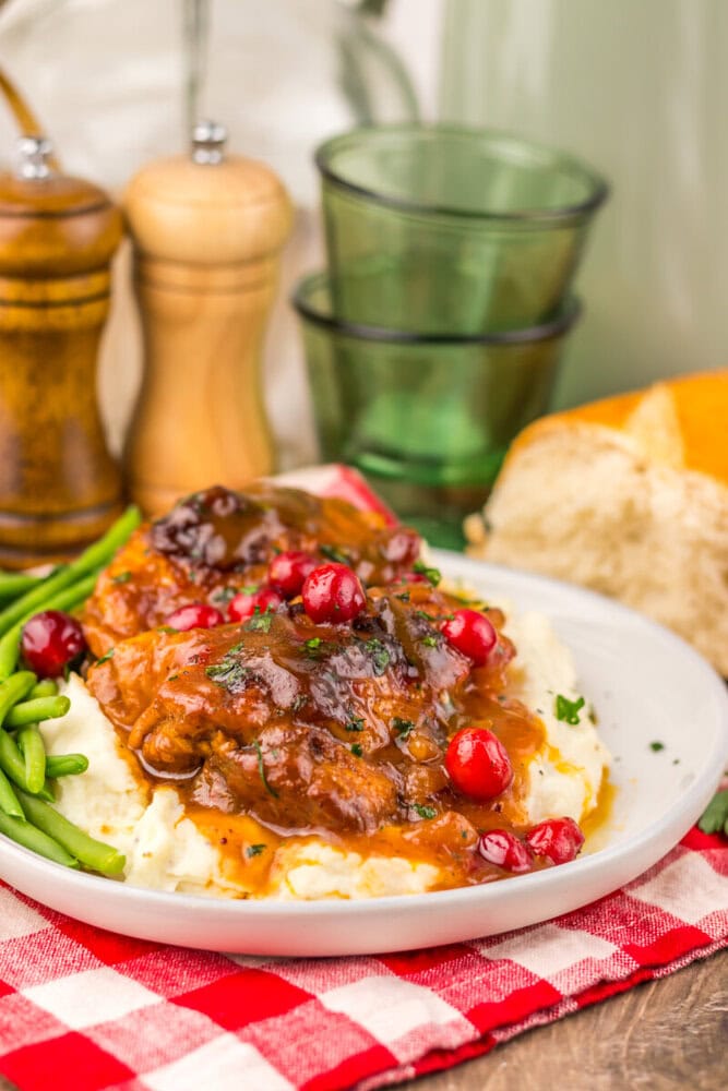 Slow cooker cranberry BBQ chicken plated over mashed potatoes with green beans and cranberry garnish