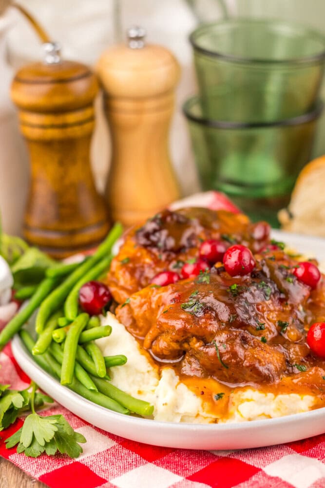 Slow cooker cranberry BBQ chicken plated with mashed potatoes and green beans, garnished with cranberries