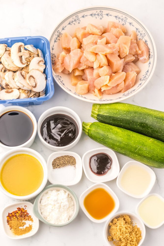 Slow cooker chicken ingredients overhead: raw chicken pieces, mushrooms, cucumbers, soy sauce, hoisin, honey, garlic, ginger, and spices in prep bowls