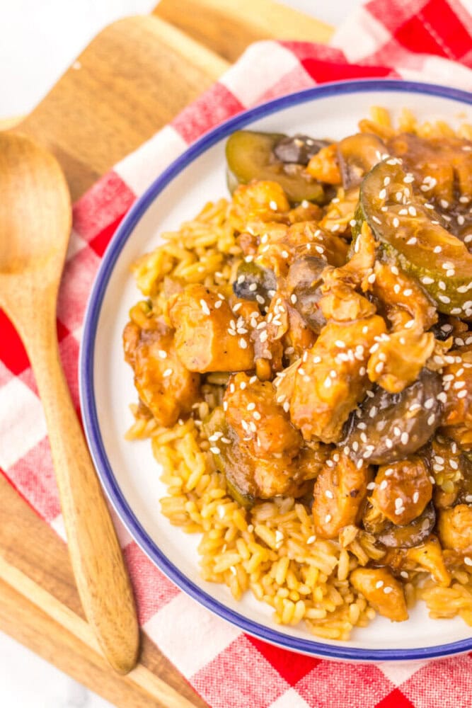 Slow cooker panda express mushroom chicken with sesame seeds served over pasta on white plate with blue rim