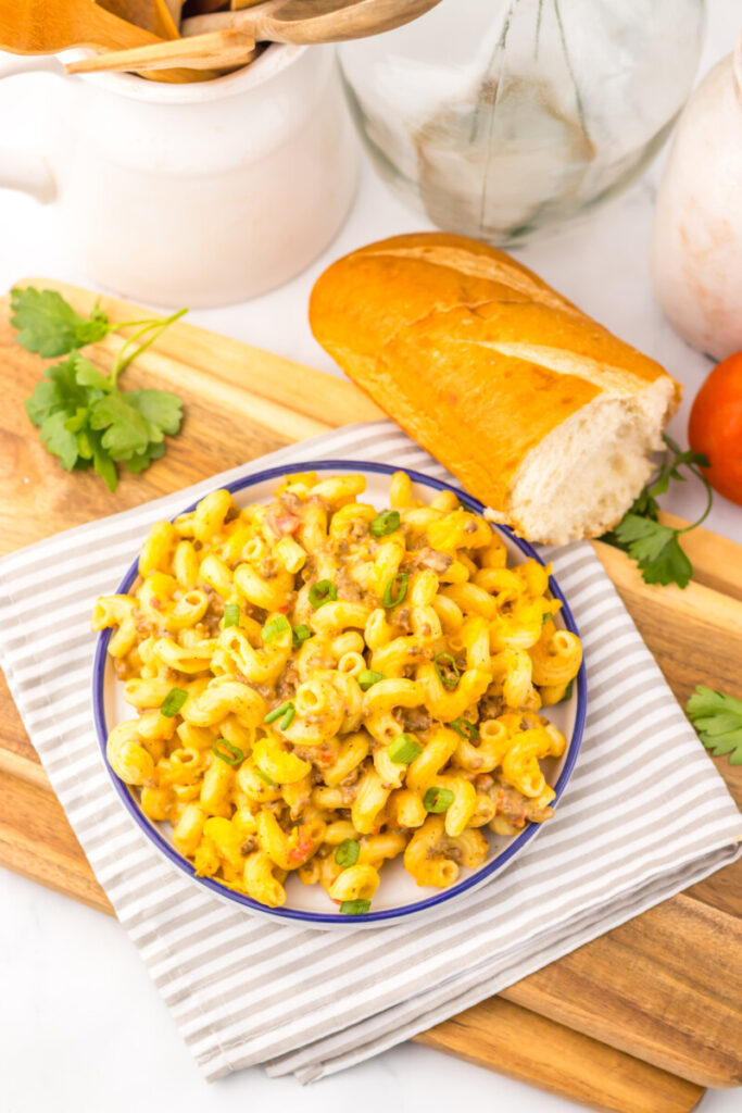 Slow cooker Rotel pasta with cheese and green onion garnish served in a blue-rimmed bowl with crusty bread and fresh cilantro