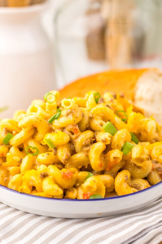 Slow cooker Rotel pasta with ground beef, corn, and green onion garnish in white serving bowl