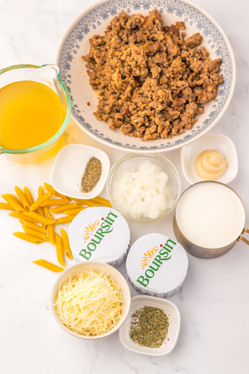 Slow cooker sausage Boursin pasta ingredients laid out including browned sausage, penne pasta, Boursin butter, broth, onions, cheese, milk and seasonings