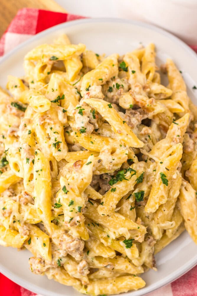 Slow cooker sausage Boursin pasta with ground meat and creamy sauce garnished with parsley on white plate