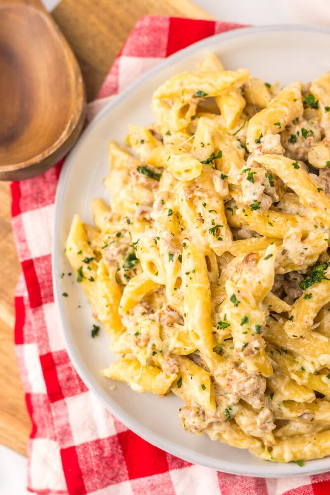 Slow cooker sausage Boursin pasta with creamy sauce and fresh parsley garnish on white plate