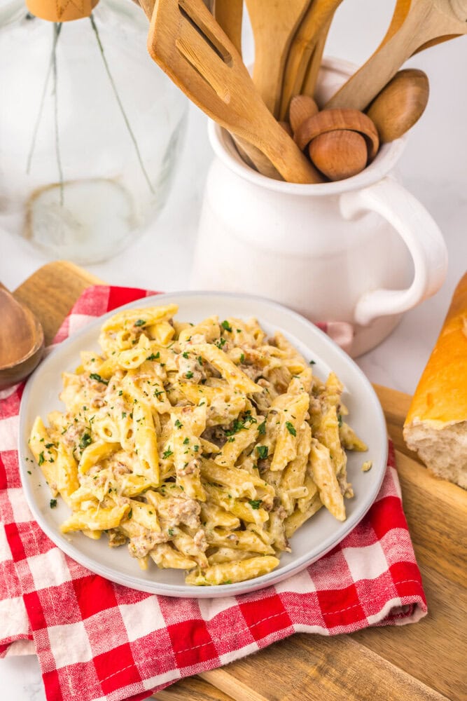 Slow cooker sausage Boursin pasta plated on white dish with herb garnish and red checkered napkin