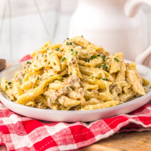 Slow cooker sausage Boursin pasta plated on white dish with parsley garnish and checkered napkin