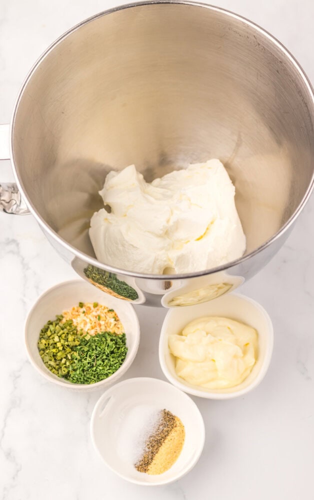 Creamy sour cream chip dip ingredients laid out before mixing - sour cream base in large bowl with green onions, corn, mayo, and seasonings in prep bowls