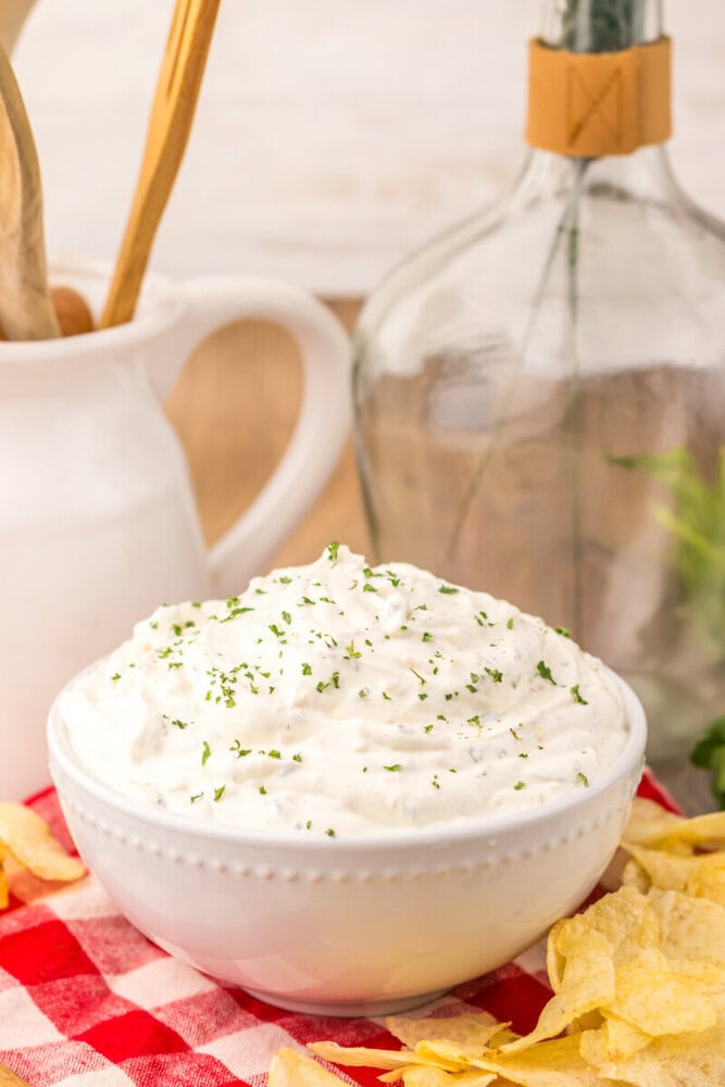 Creamy sour cream chip dip in white bowl garnished with chives, served with potato chips