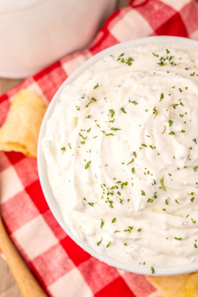 Creamy sour cream chip dip in white bowl garnished with chives on red checkered cloth