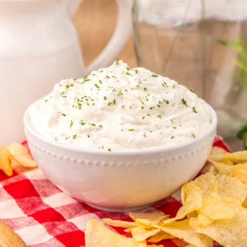 Creamy sour cream chip dip topped with chives served with potato chips and fresh herbs