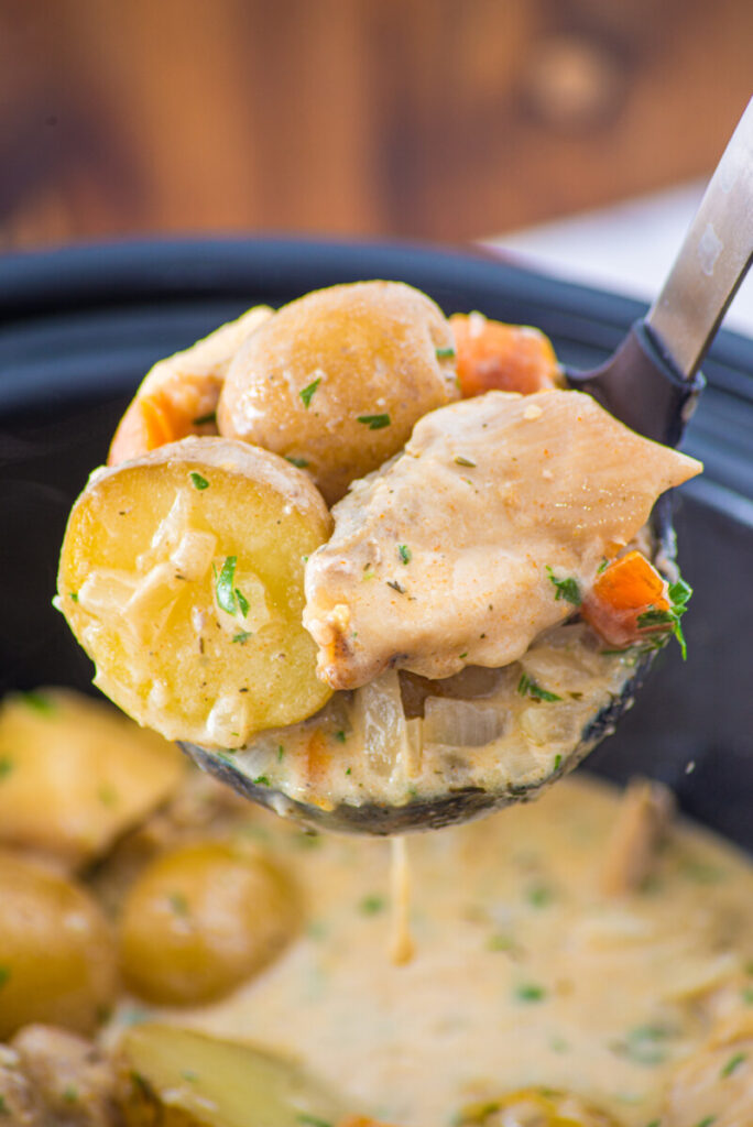 Creamy slow cooker chicken and potatoes on a spoon over pot, garnished with chives