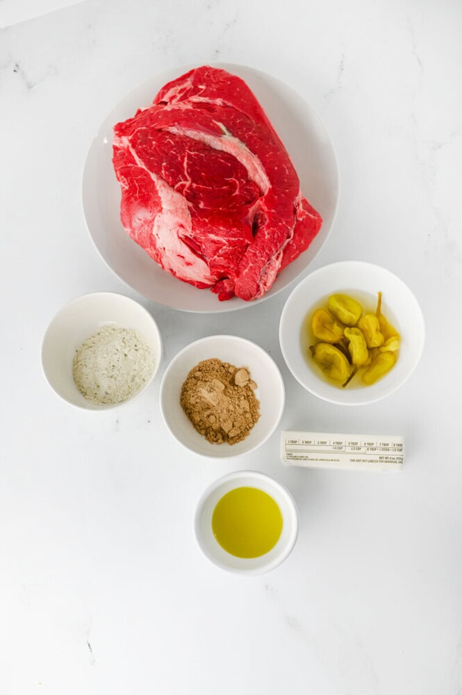 Mississippi pot roast ingredients laid out in bowls: raw beef roast, salt, spices, pepperoncini peppers, and olive oil